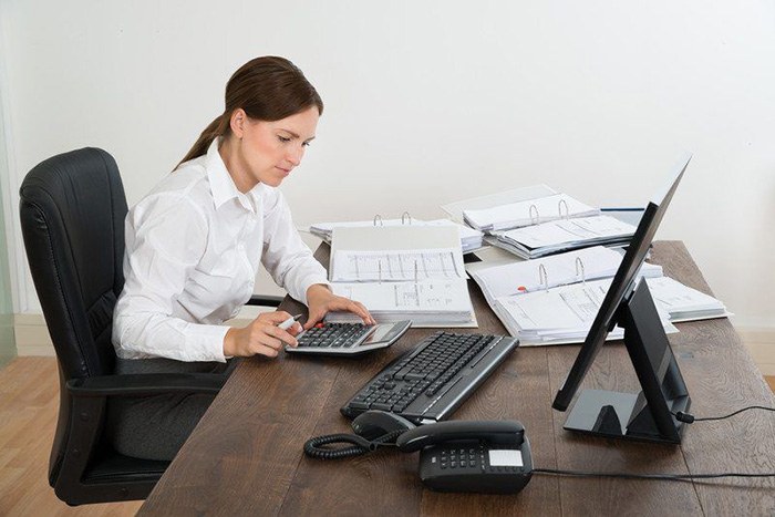 一个女人在她的办公桌前忙着在计算器上加数字，这是一个亚斯伯格症患者工作的例子