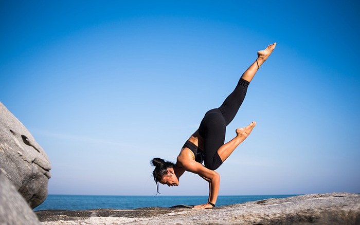 Woman on a rock with the ocean in the background doing yoga as an example of jobs in kinesiology