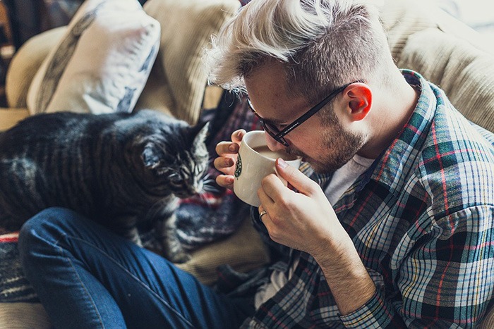 Man relaxing on couch with his cat sipping a cup of coffee as an example of low-stress jobs