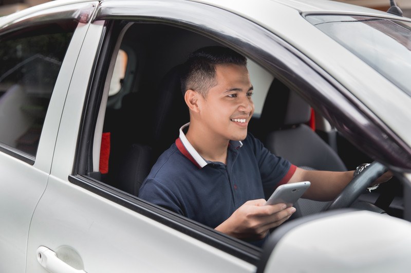 Image of a young man in a silver car using his phone