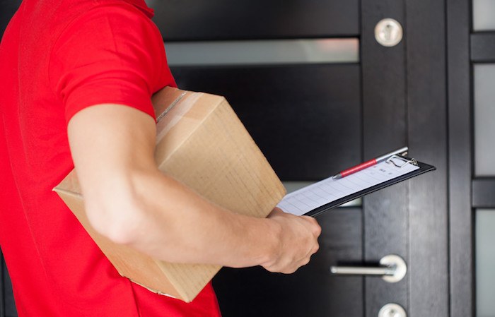 man with red polo shirt and package under arm with form to sign. he is working a package delivery gig from an app making money