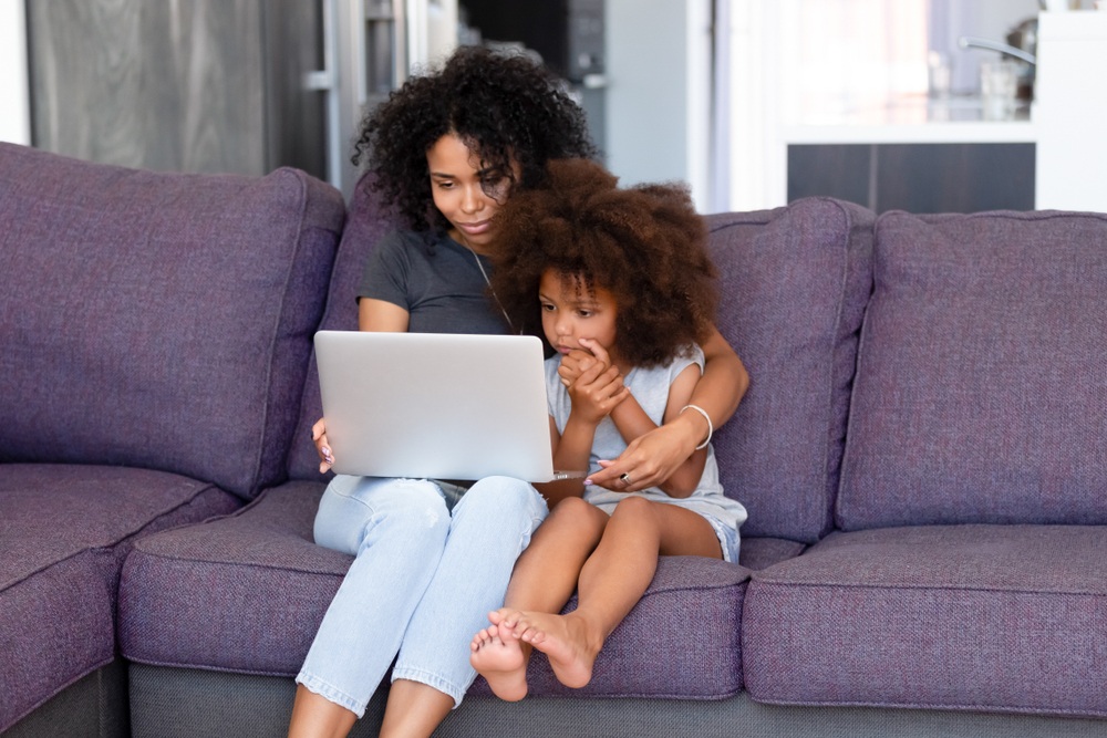 非裔美国母亲带着孩子在沙发上用笔记本电脑写博客