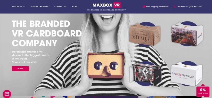 这张MaxBox VR的主页截图有一个深蓝色的导航栏，上面有一个白色的文字，上面是一张黑白照片，一个微笑的金发女人拿着一个纸板VR观看器，还有白色的文字描述由MaxBox VR制作的纸板观看器。