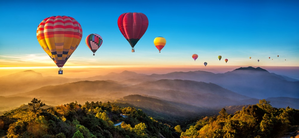 colorful hot air balloons floating over sunset mountains