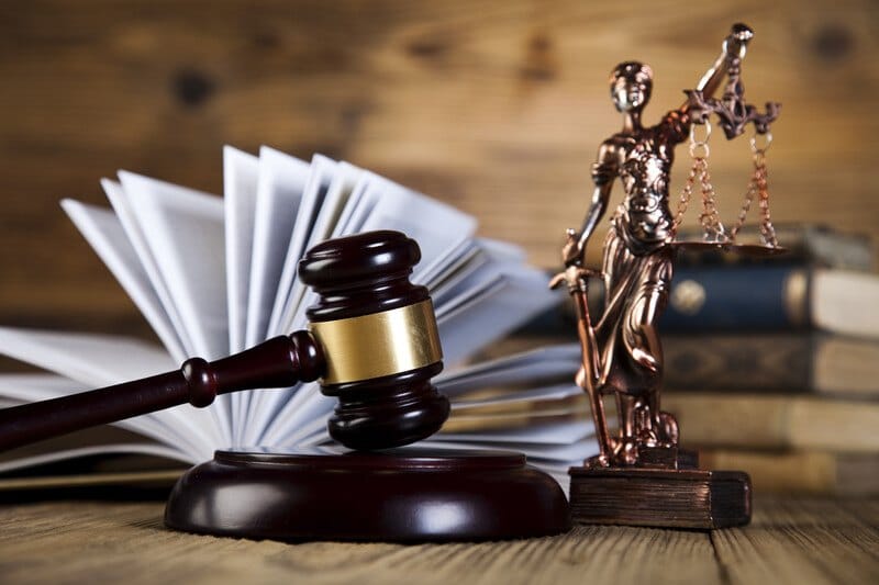 This photo shows a gavel, an open book, and a bronze figurine of a woman holding a sword and a set of scales, representing the best legal affiliate programs.