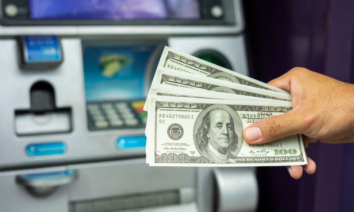A man is holding a wad of cash in front of an ATM