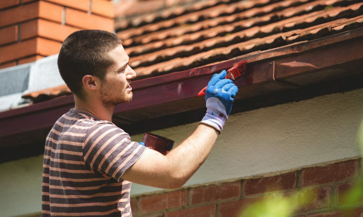A smiling man working for Taskrabbit paints a house on a sunny day.
