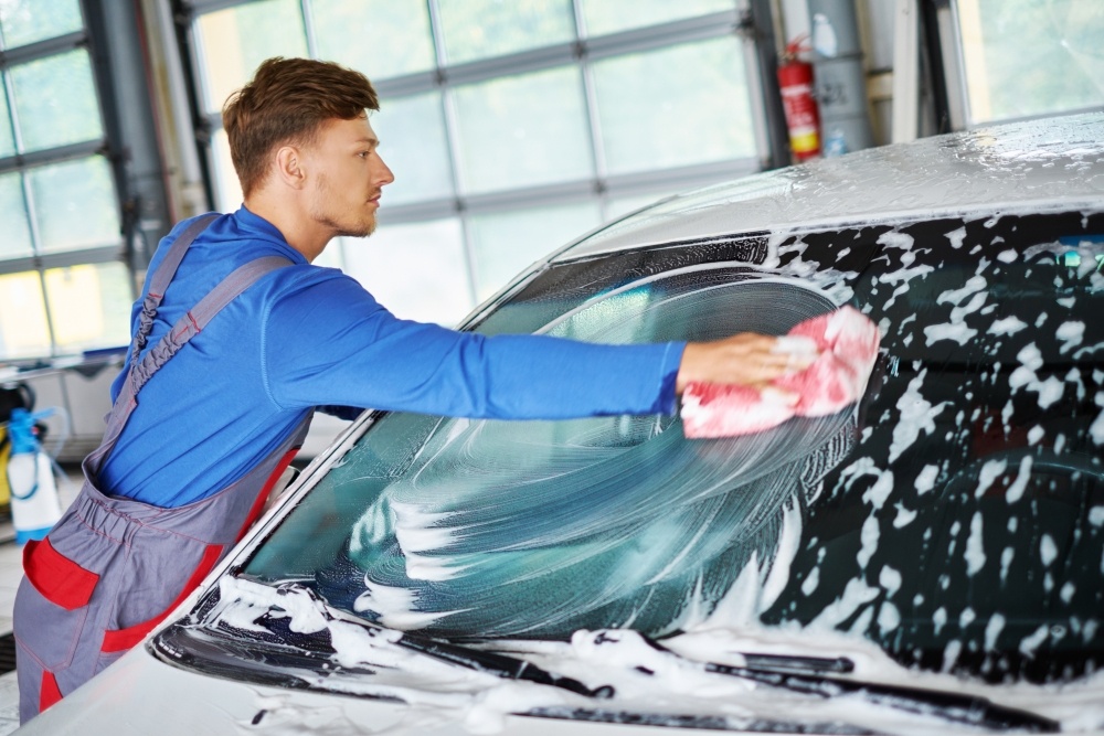穿着工作服的年轻人正在手洗汽车的挡风玻璃