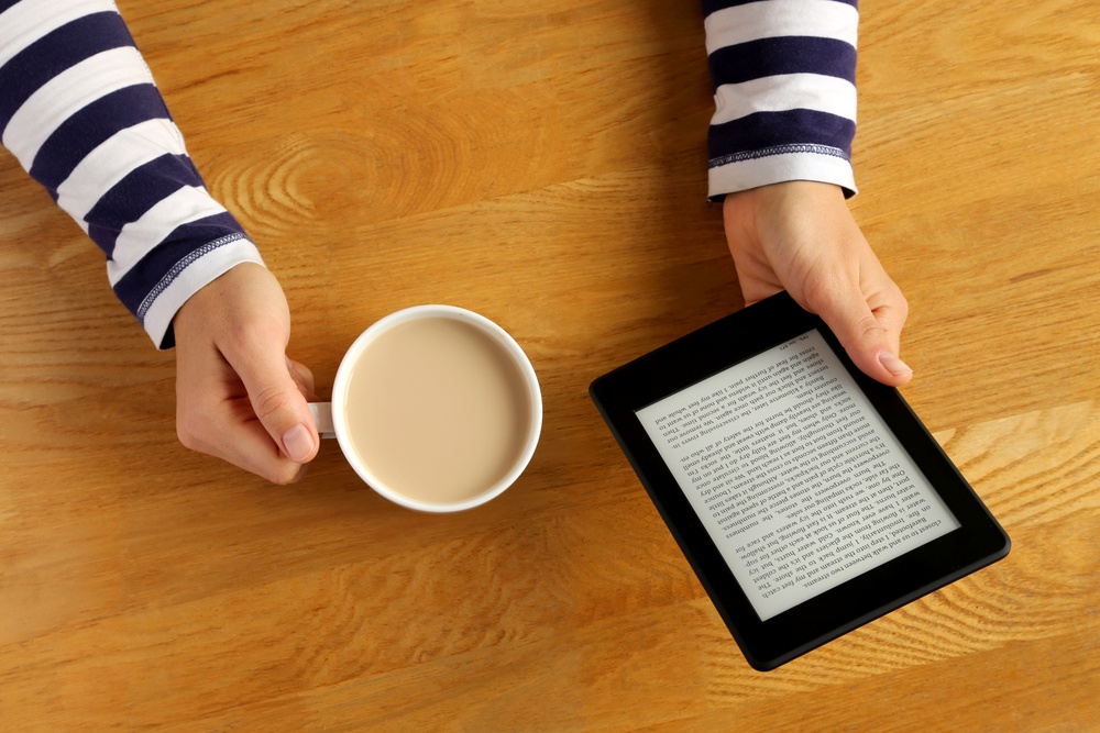 A pair of hands holding a cup of coffee and a Kindle