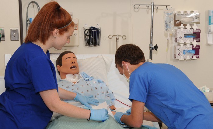 Two nursing students practicing their skills on a dummy in a patient bed as an example of jobs for nursing students