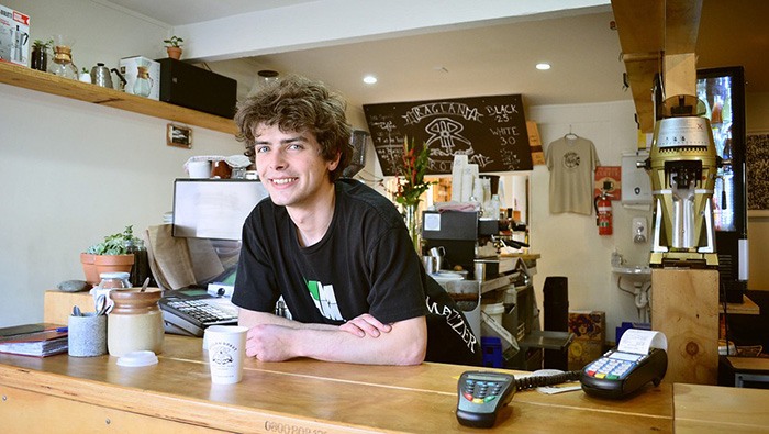 Young man smiling working the counter at a coffee shop representing a job for younger people
