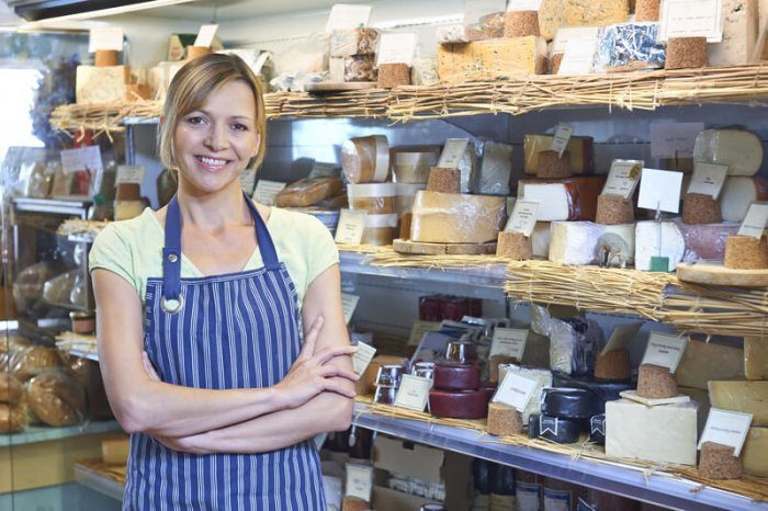 woman standing next to various types of cheese in a small local business