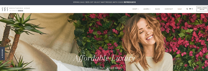 Brentwood Home网站截图，显示一个年轻的棕色头发的女人在花卉背景。她咧着嘴笑，闭着眼睛。