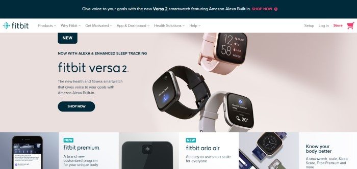 This screenshot of the home page for Fitbit shows three Fitbit Versa 2 smartwatches in pink, black, and gray over a beige background, near a section of black text describing the device, along with a black 