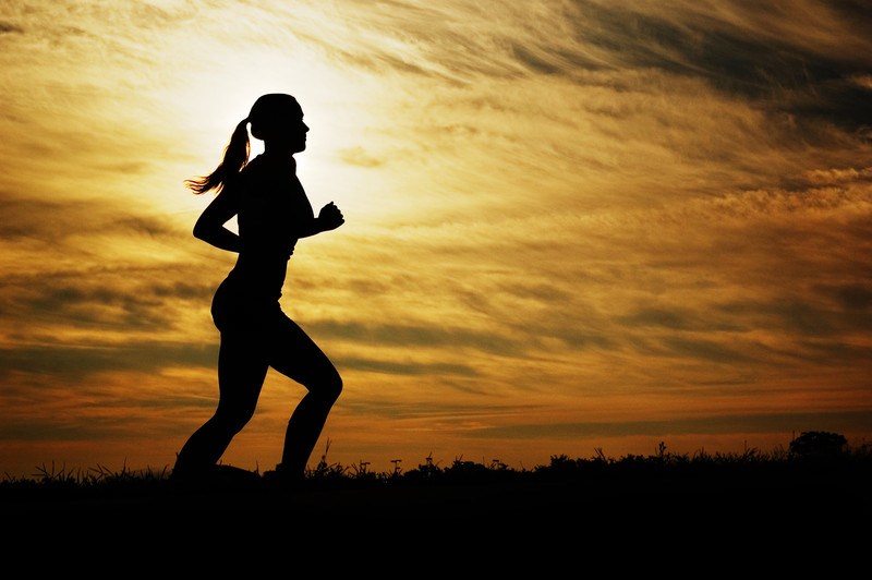 This photo shows the silhouette of a woman in a ponytail running against a yellow and orange sunset, representing the best women's fitness affiliate programs.