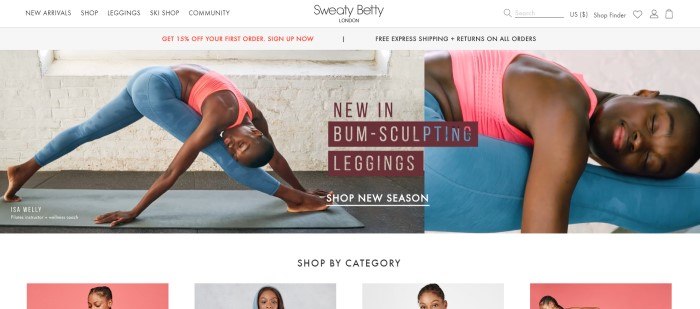 This screenshot of the home page for Sweaty Betty shows a dark-skinned woman in a pink sports bra and blue sculpting leggings stretching on a yoga mat in front of a white-painted brick wall.