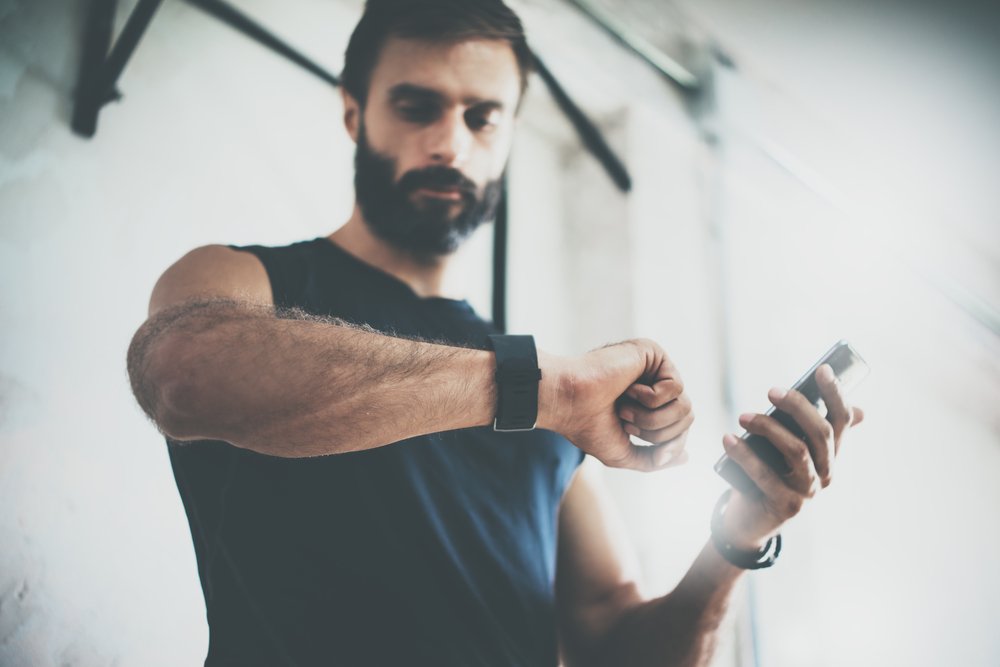 bearded man looking at fitness watch and smartphone