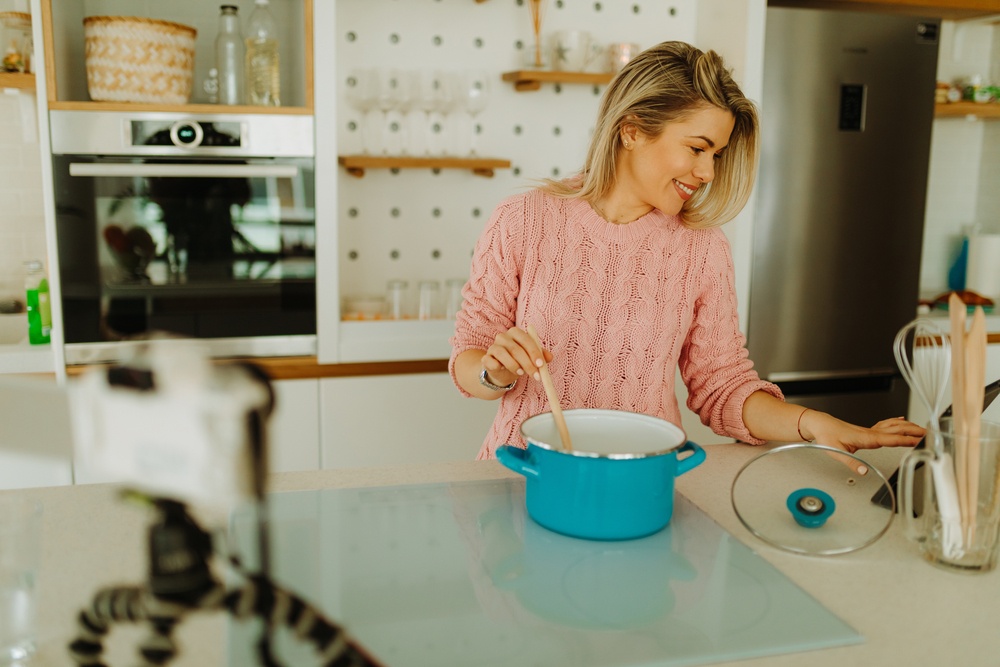 young blond woman using teal cookware and searching for online recipe on iPad
