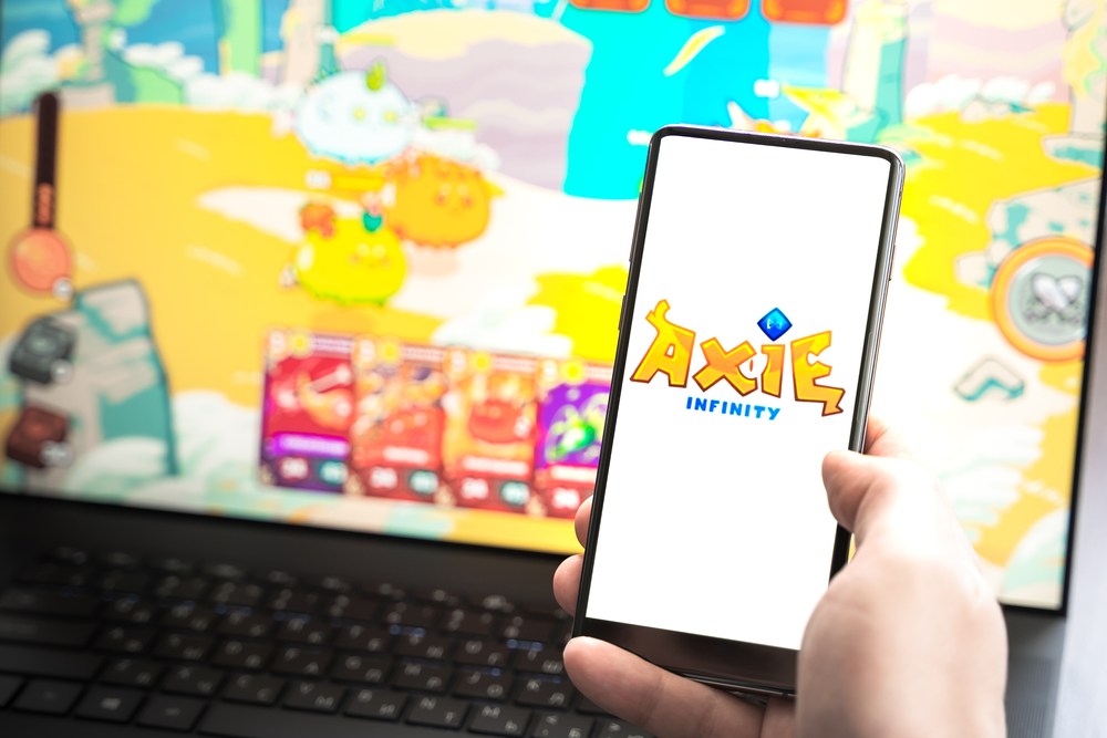 mobile phone playing axie infinity game with laptop axie infinity gameplay in background