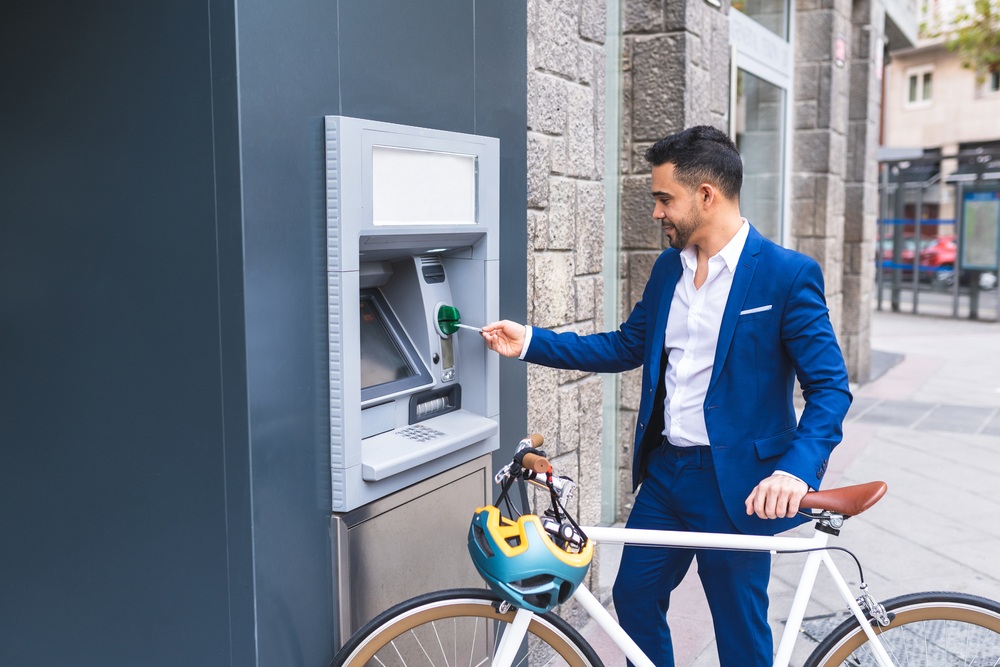 一个米an with a bike inserts a card into an ATM while smiling.