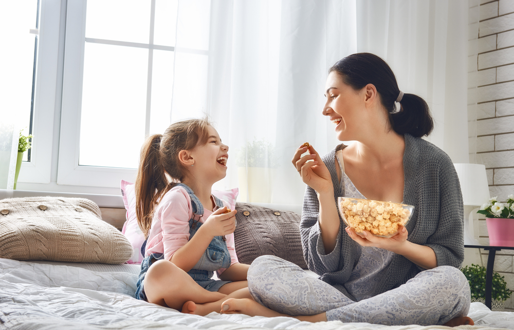 一个女人和一个孩子坐在床上吃着碗里的爆米花，笑得很开心。
