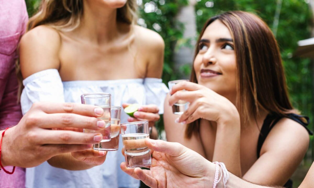 A group of smiling women toast with glasses of tequila and limes.