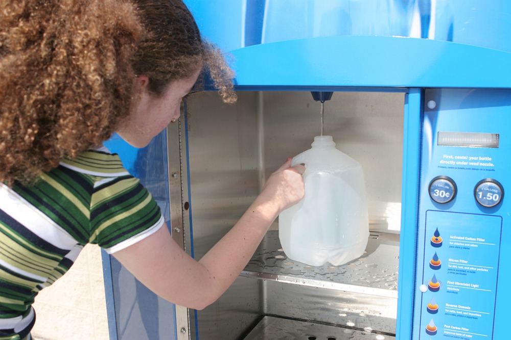 A girl uses a vending machine to fill up a jug of water.