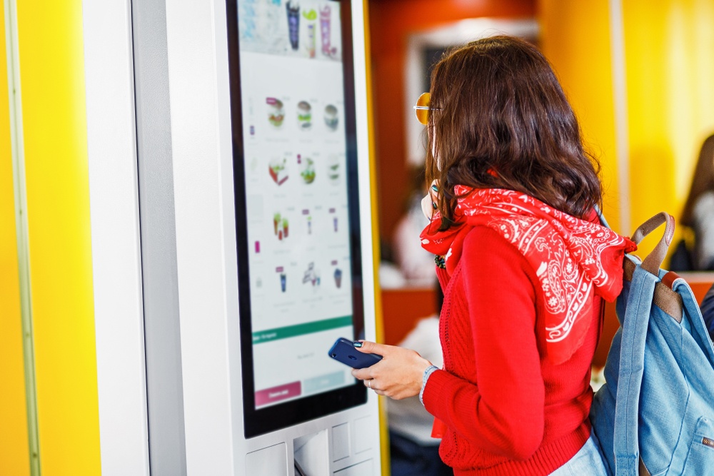 A woman in sunglasses chooses a full hot meal at a vending machine.