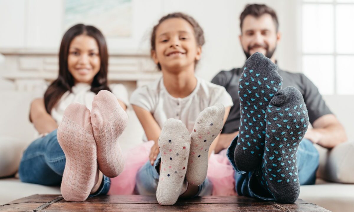 A man, woman, and child show off their socks with their feet on the table.