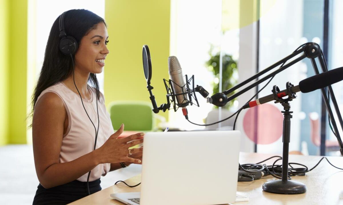 A woman near a laptop and a microphone records a podcast.