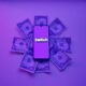 twitch logo on mobile phone resting on pile of dollar bills with purple background and overlay