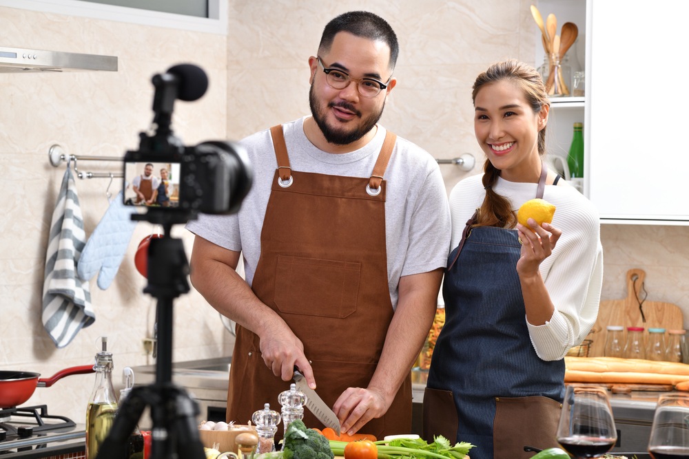 young couple cooking in front of a camera for their YouTube channel